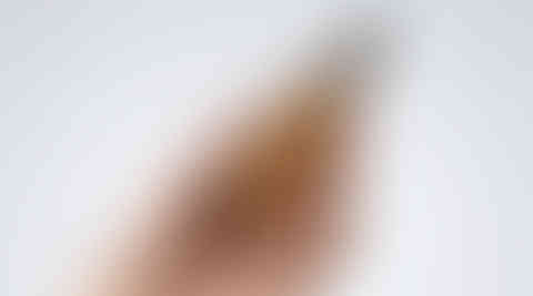 Hand holding amber dropper bottle against plain background.
