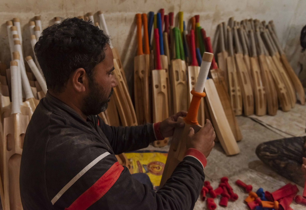 A worker puts the rubber grip on the wooden handle