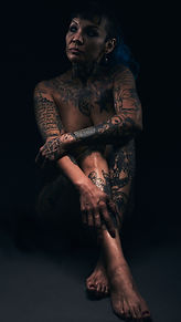 Fine art nude portrait photography of tattooed woman sitting on floor looking to side. Retrato desnudo artistico de mujer tatuada y desnudo sentada en el suela/piso viendo a un costado