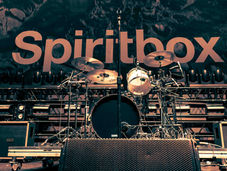 Empty concert stage with a drum kit and microphones in front of a large Spiritbox backdrop