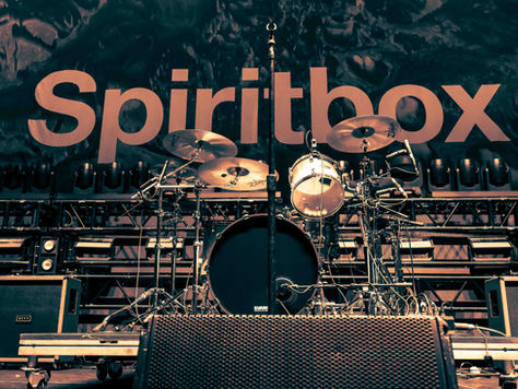 Empty concert stage with a drum kit and microphones in front of a large Spiritbox backdrop