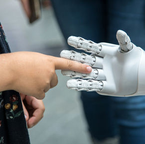 a child reaching out a finger into the palm of a robot's hand