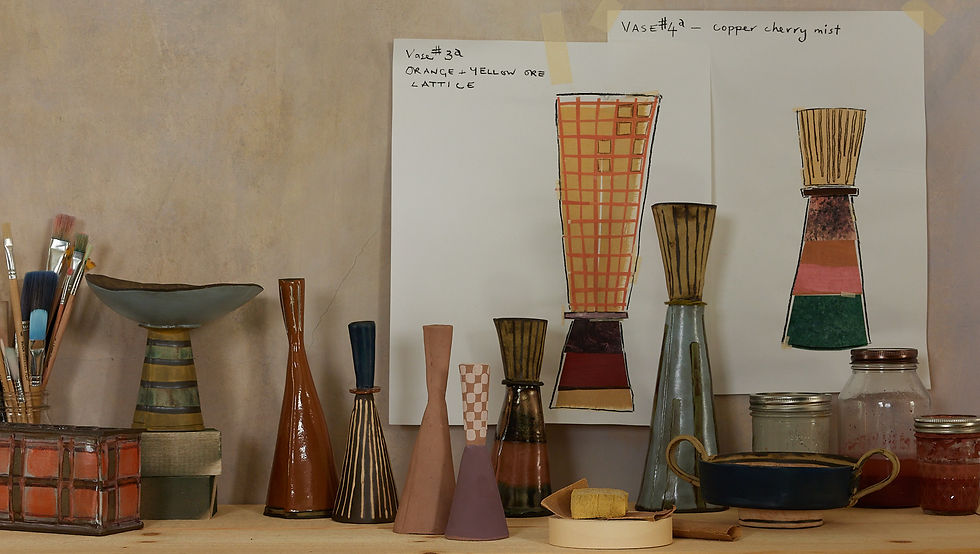 Drawings and plans of candlesticks taped to a wall, with the finished products on the table below it.