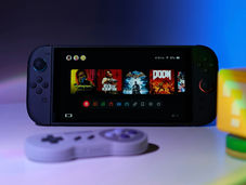 A Nintendo Switch 2 home screen showing Cyberpunk, Red Dead Redemption, Batman Arkham Asylum, and Doom icons. A grey SNES controller is in the foreground and a Mario ? block is on the right, both are blurry.