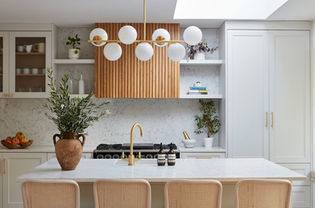 Light kitchen with white cabinets, brass faucet, wooden accent, and modern pendant lighting.