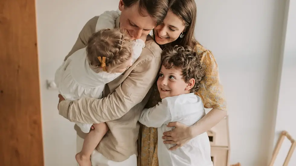 Family embraces joyfully in a bright room; adults and children sharing warmth.