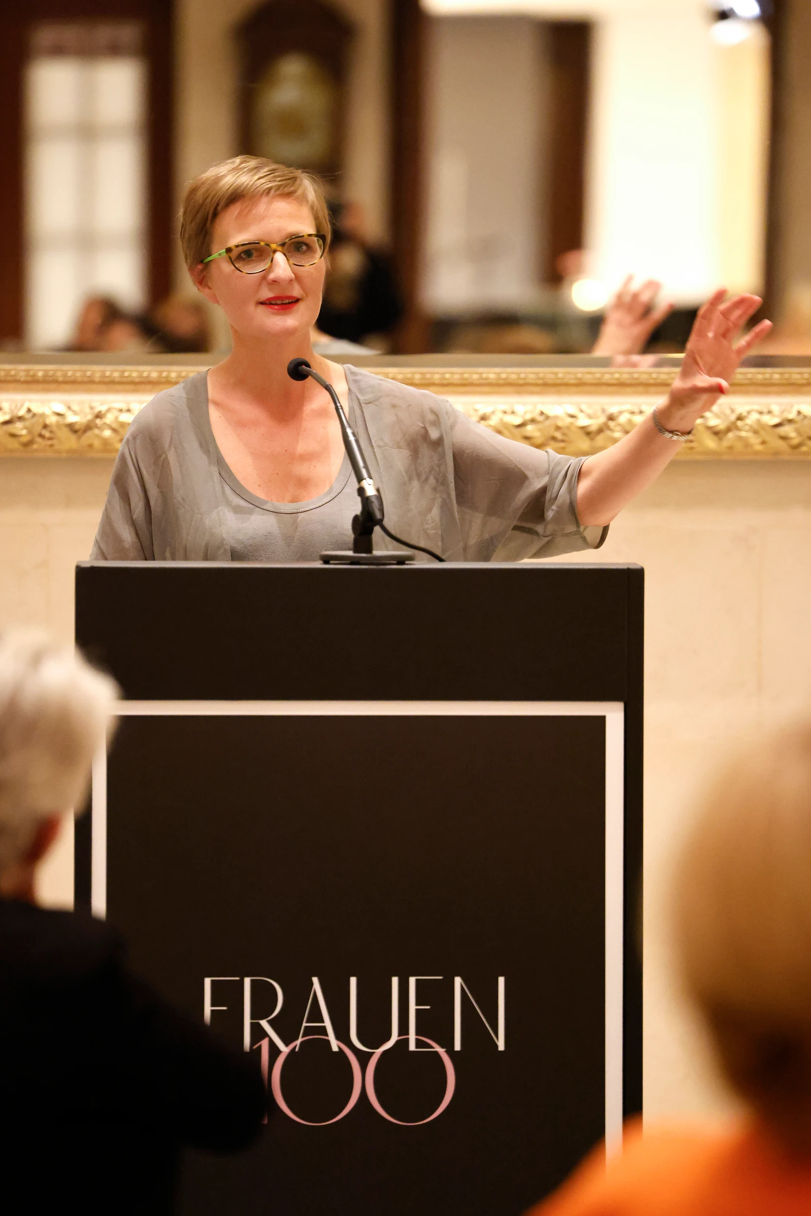 Frau mit Brille steht am Rednerpult und gestikuliert mit der Hand während einer Rede.