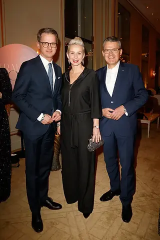 Drei Personen in eleganter Abendkleidung stehen nebeneinander bei einer Veranstaltung und schauen in die Kamera.