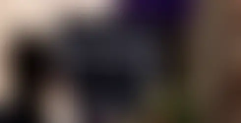 Eine Frau steht an einem Rednerpult, hält ein Mikrofon und spricht vor einem Publikum, während im Vordergrund gedeckte Tische zu sehen sind.