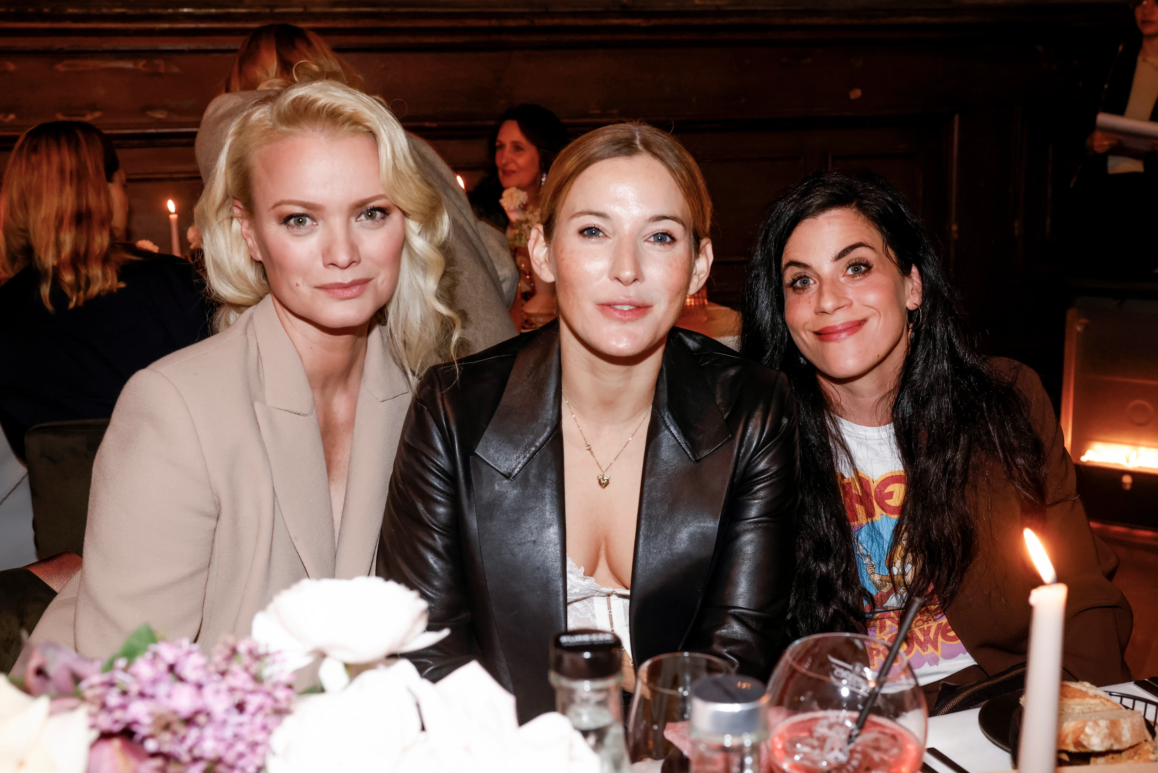 Drei Frauen sitzen gemeinsam bei einem Dinner-Event und lächeln in die Kamera.