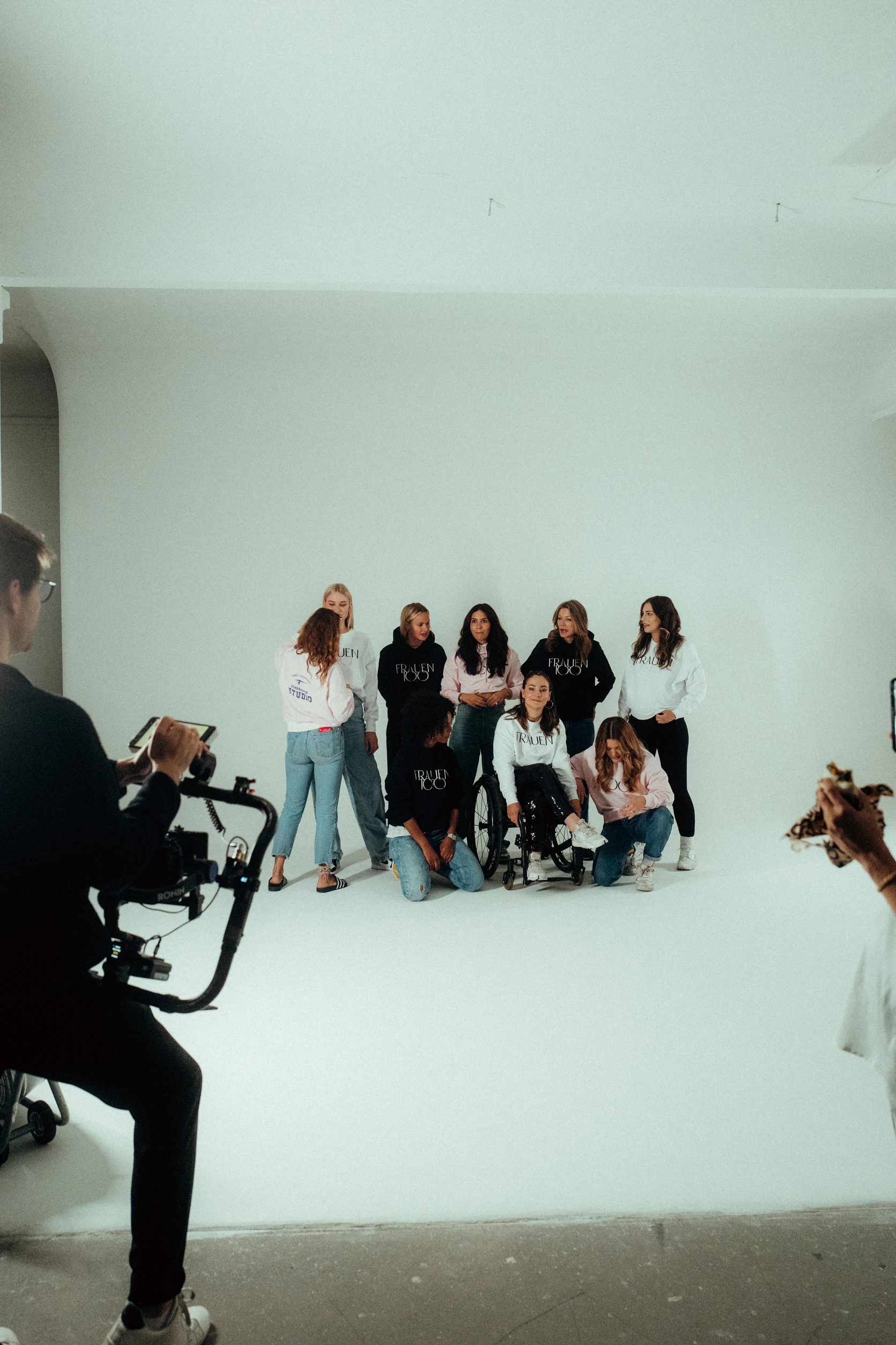 Blick hinter die Kulissen eines Shootings: Kamerateam filmt eine diverse Gruppe von Frauen im Studio, eine sitzt im Rollstuhl im Mittelpunkt.