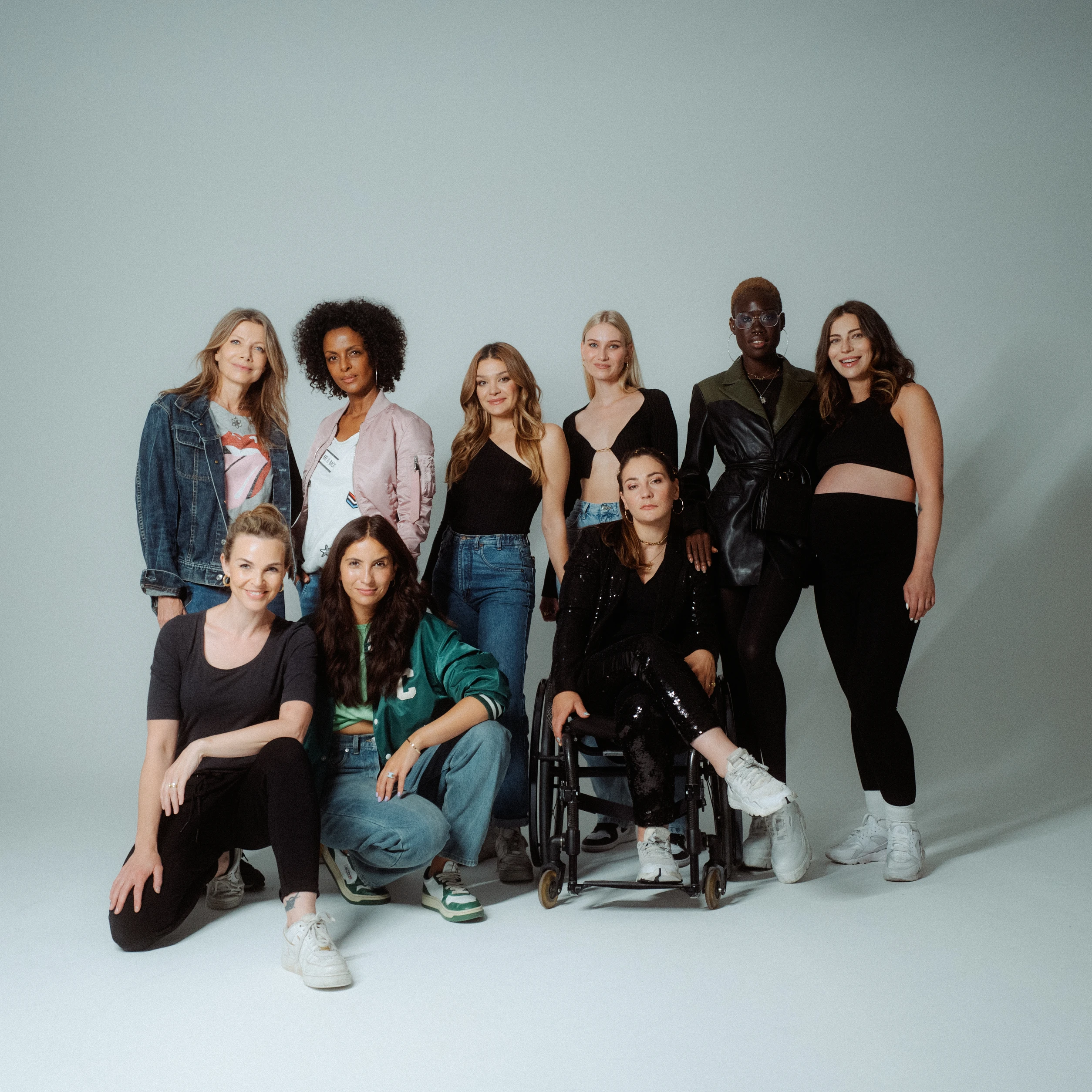 Diverse Gruppe von Frauen posiert gemeinsam im Studio vor hellem Hintergrund, eine Frau sitzt im Rollstuhl.