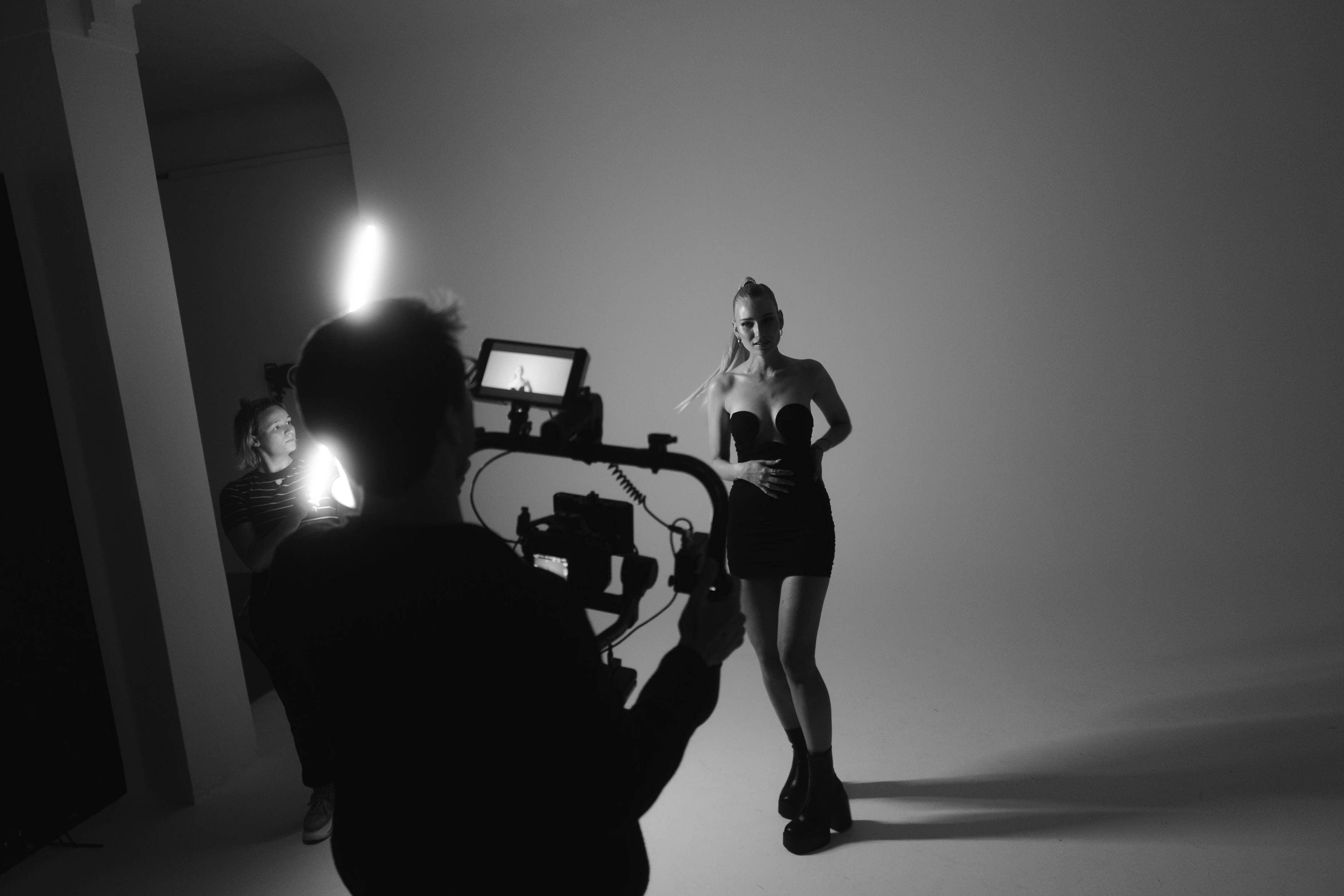 Blick hinter die Kulissen eines Shootings: Kamerateam filmt eine Frau im schwarzen Outfit vor Studiohintergrund.