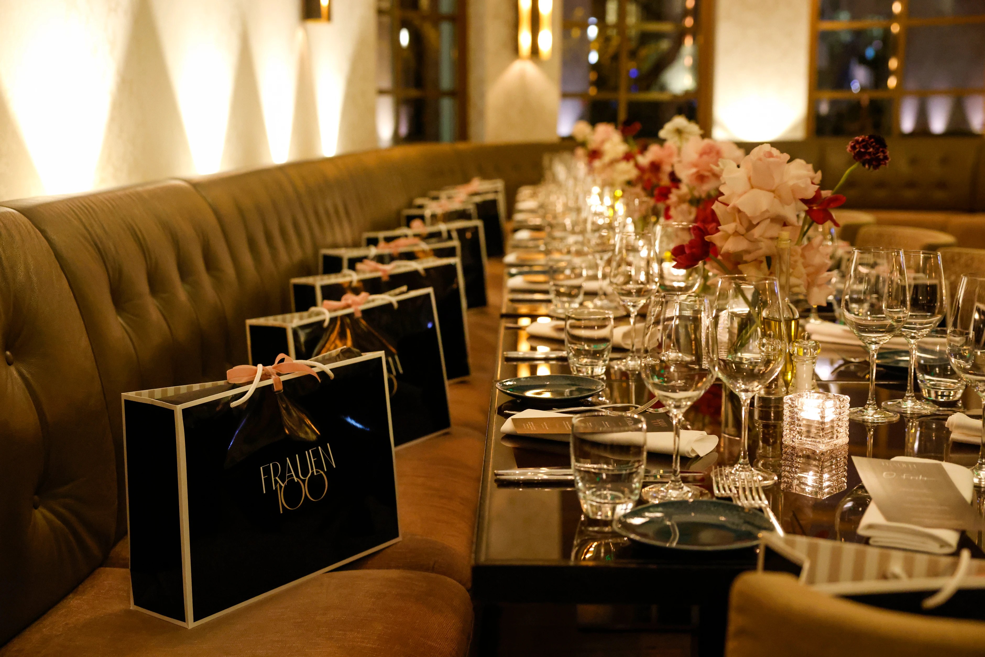 Lange festlich gedeckte Tafel mit Blumen, Kerzen und Gläsern; auf den Sitzplätzen liegen Geschenktaschen mit „Frauen100“-Logo.