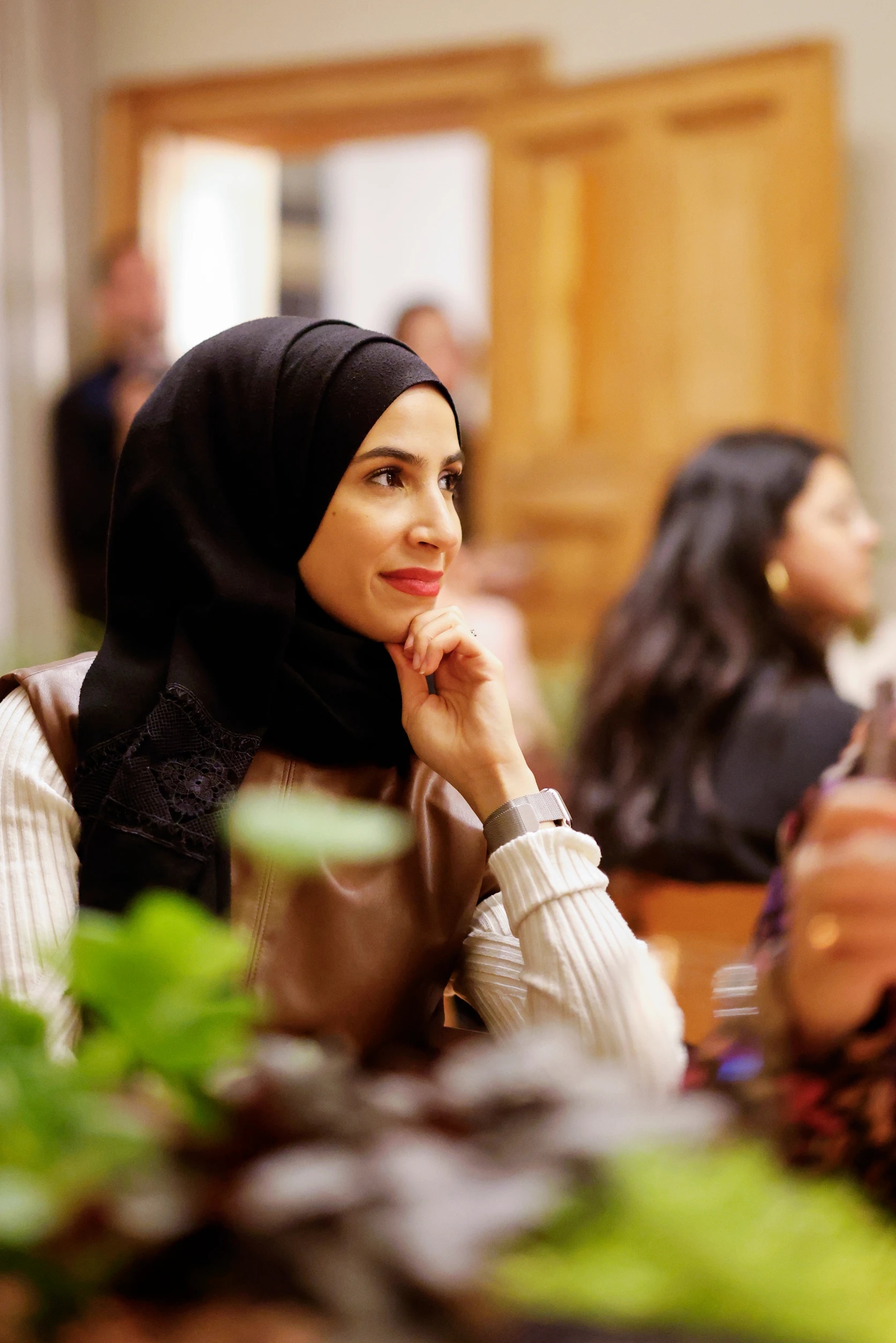 Eine Frau mit schwarzem Hijab sitzt aufmerksam an einem Tisch und hört konzentriert zu.