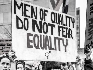 Schwarz-weißes Foto einer Demonstration: Mehrere Personen halten ein Schild mit der Aufschrift „Men of quality do not fear equality“.
