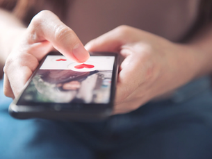 Nahaufnahme von Händen, die auf einem Smartphone eine Dating-App bedienen und ein Profil mit Herzsymbol nach rechts wischen.