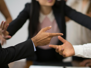 Mehrere Personen in Businesskleidung gestikulieren mit den Händen in einer hitzigen Diskussion, während eine Frau im Hintergrund versucht, zu schlichten.