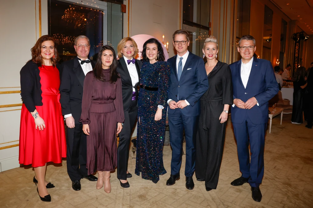 Gruppe von acht Personen in Abendgarderobe steht gemeinsam in einem festlich beleuchteten Raum und posiert für ein Gruppenfoto.