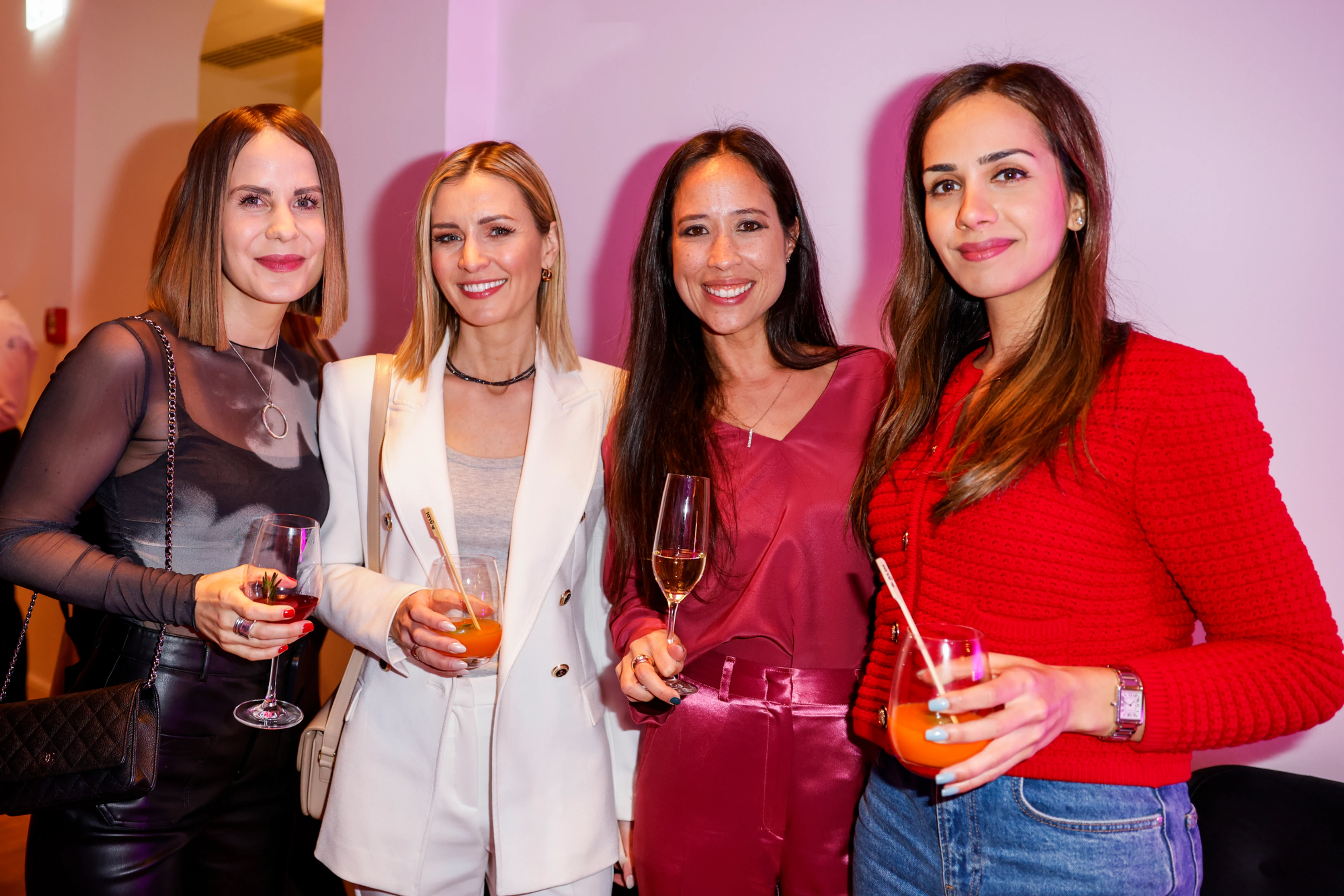 Vier Frauen stehen eng beieinander, lachen in die Kamera und stoßen mit Drinks an – ein klassischer Networking-Moment mit entspannter, eleganter Atmosphäre.