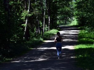 Person joggt auf einem schattigen Waldweg, umgeben von Bäumen und Sonnenlicht, das durch die Blätter fällt.