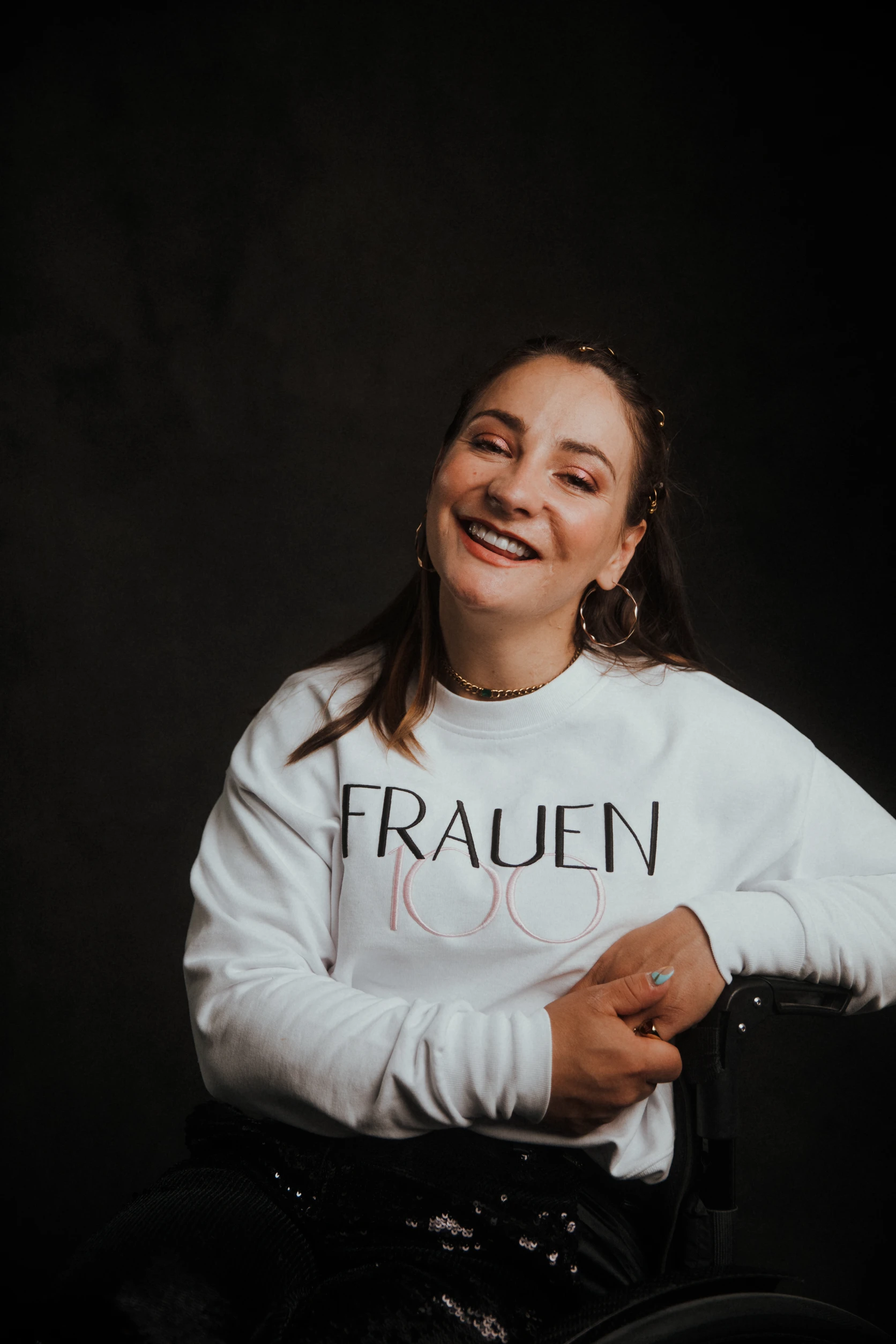 Frau im Rollstuhl lächelt in die Kamera und trägt ein „Frauen100“-Sweatshirt.