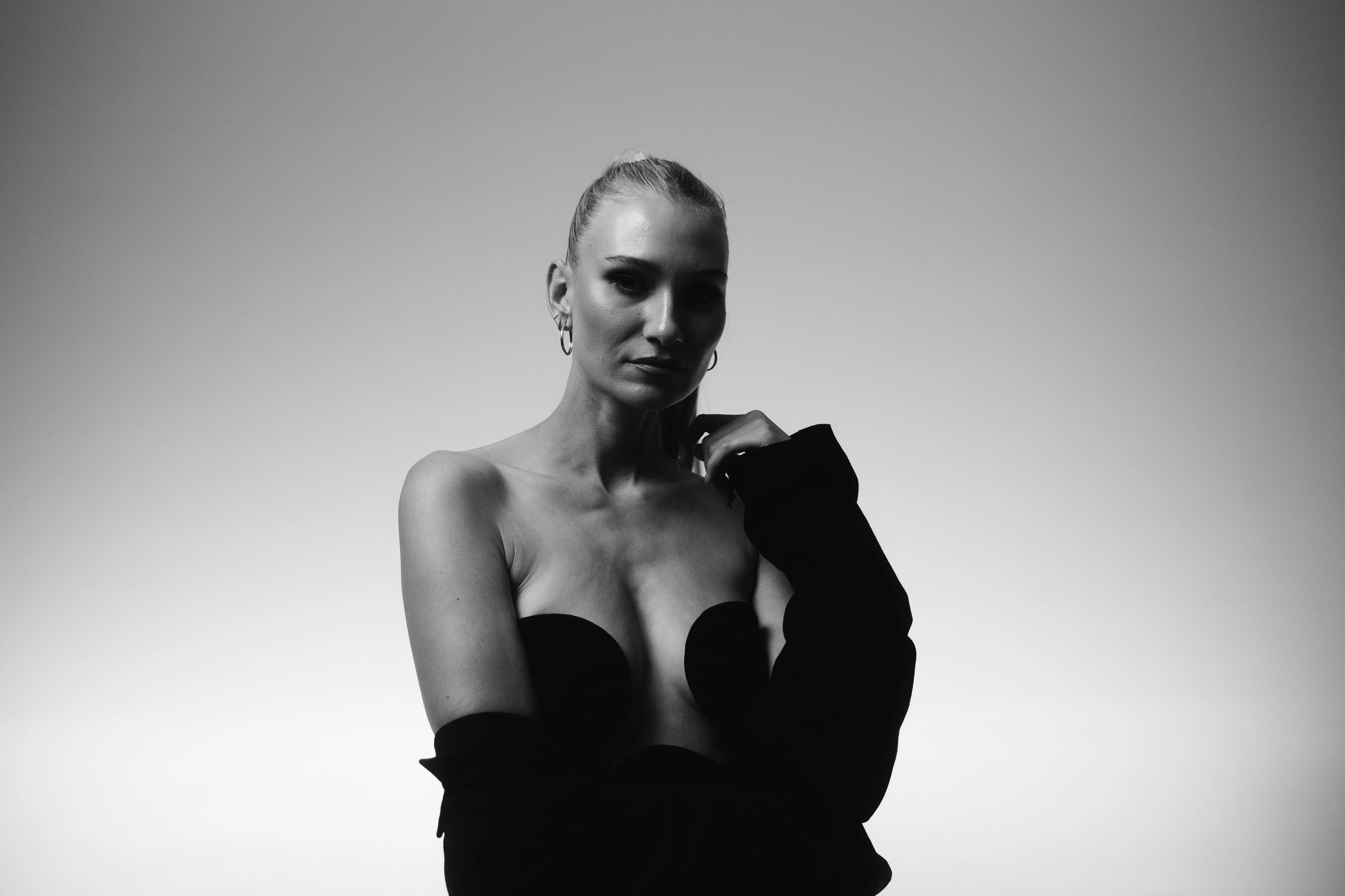 Schwarz-weiß Porträt einer Frau in elegantem Outfit mit ernstem Blick vor hellem Hintergrund.