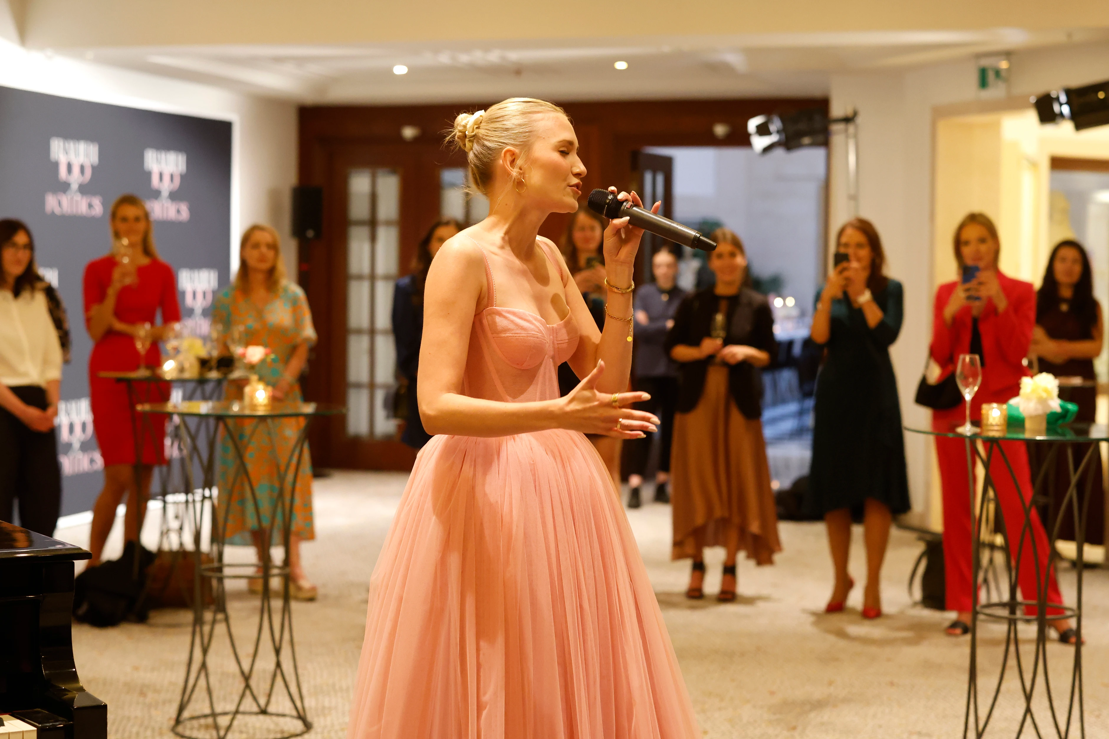 Sängerin in rosa Kleid performt vor Publikum in einem Innenraum bei einem Event.