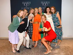 Gruppe von Frauen posiert lachend für ein gemeinsames Foto vor einer „Frauen100 & Politics“-Fotowand, eine Frau macht ein Selfie.