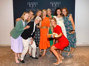 Gruppe von Frauen posiert lachend für ein gemeinsames Foto vor einer „Frauen100 & Politics“-Fotowand, eine Frau macht ein Selfie.