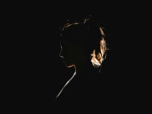 Seitliches Profil einer Frau als Silhouette vor schwarzem Hintergrund, nur von hinten leicht beleuchtet.