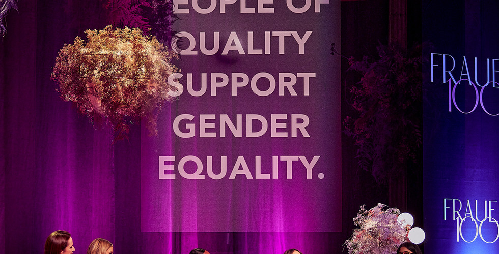 Mehrere Frauen sitzen auf einer Bühne in einer Panelrunde und diskutieren vor Publikum, während im Hintergrund „People of Quality support Gender Equality“ steht.