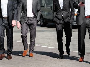 Mehrere Männer in Business-Anzügen gehen gemeinsam über eine Straße in einer Stadt.