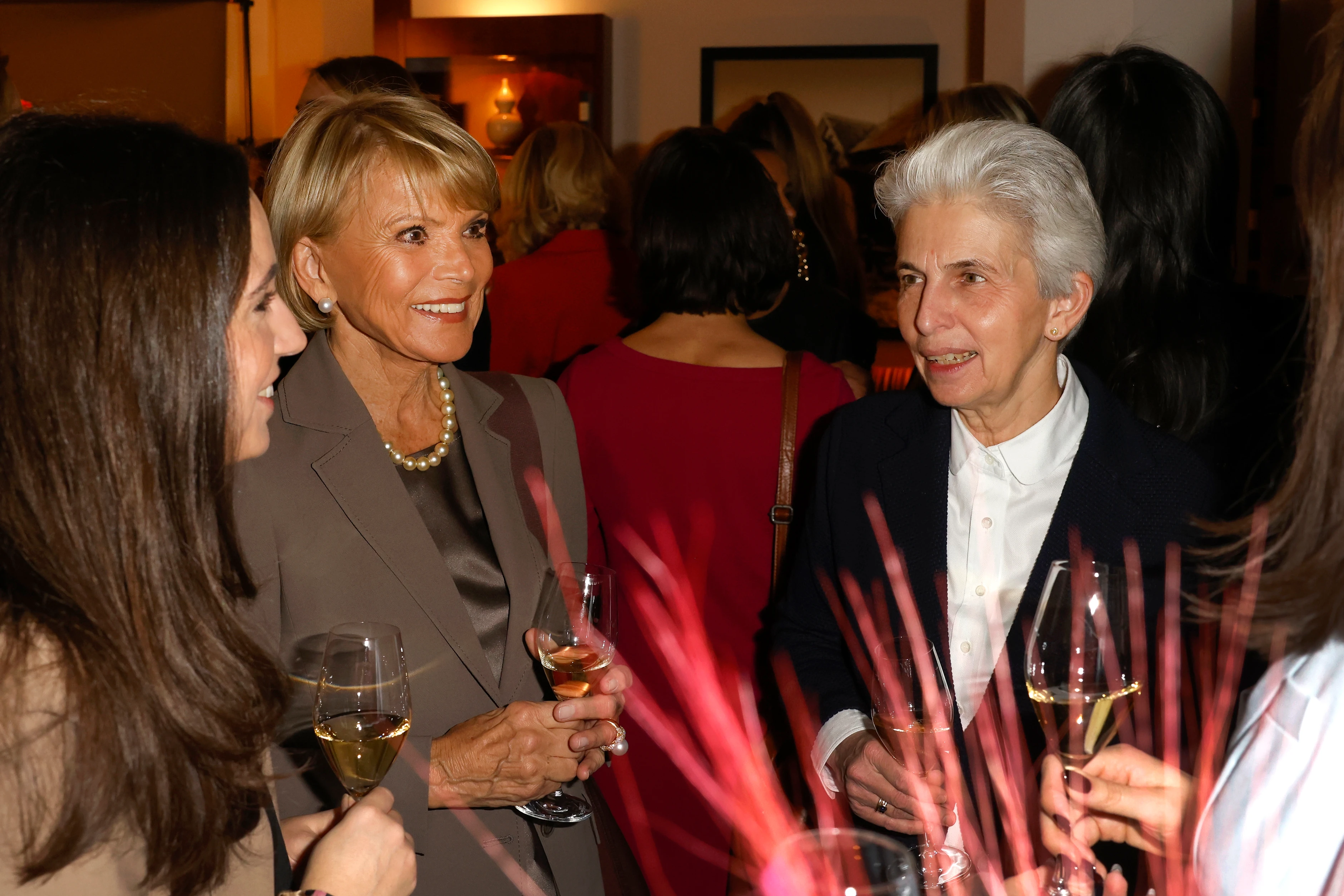 Mehrere Frauen stehen zusammen, stoßen mit Weingläsern an und unterhalten sich in entspannter Atmosphäre.