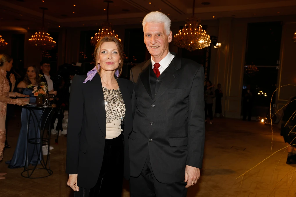 Frau und Mann stehen gemeinsam bei einem Event in einem festlich beleuchteten Raum und posieren für ein Foto.
