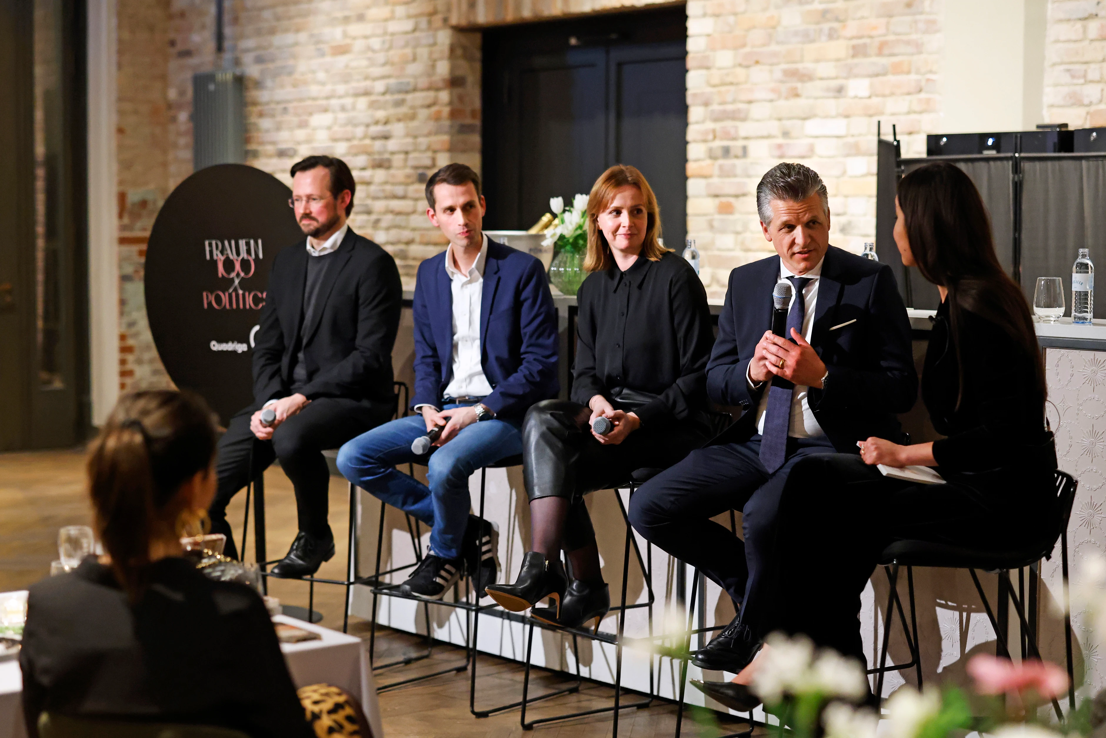 Mehrere Personen sitzen auf einer Bühne, halten Mikrofone und diskutieren im Rahmen einer Panelrunde vor Publikum.
