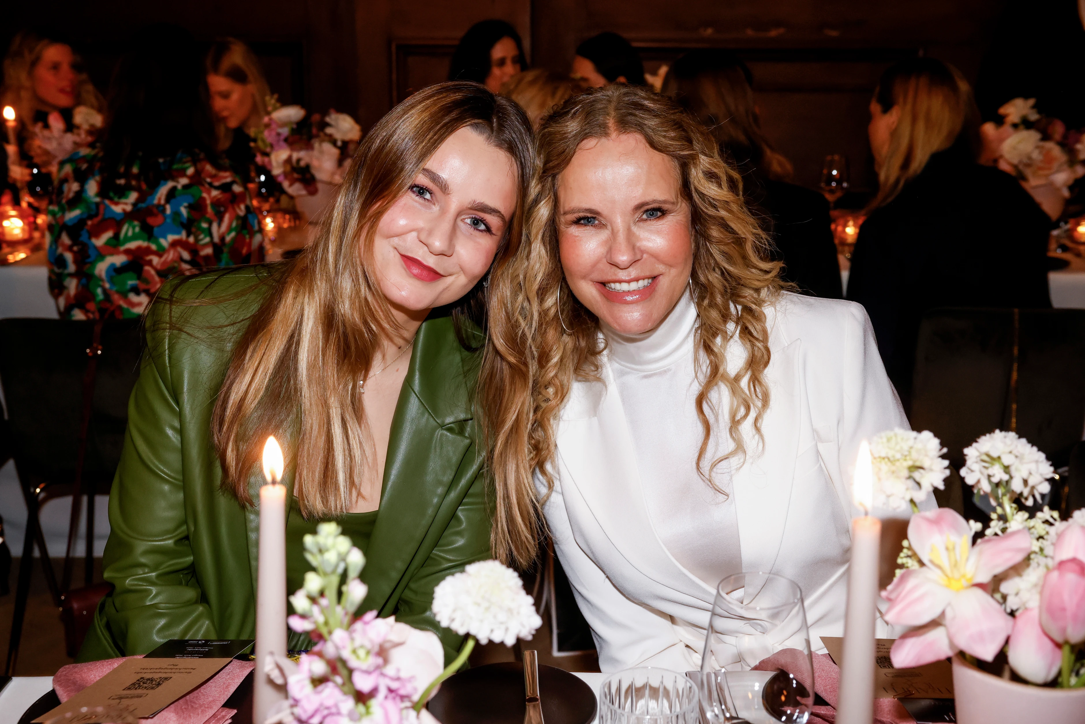 Zwei Frauen sitzen bei einem Dinner-Event zusammen und lächeln in die Kamera.