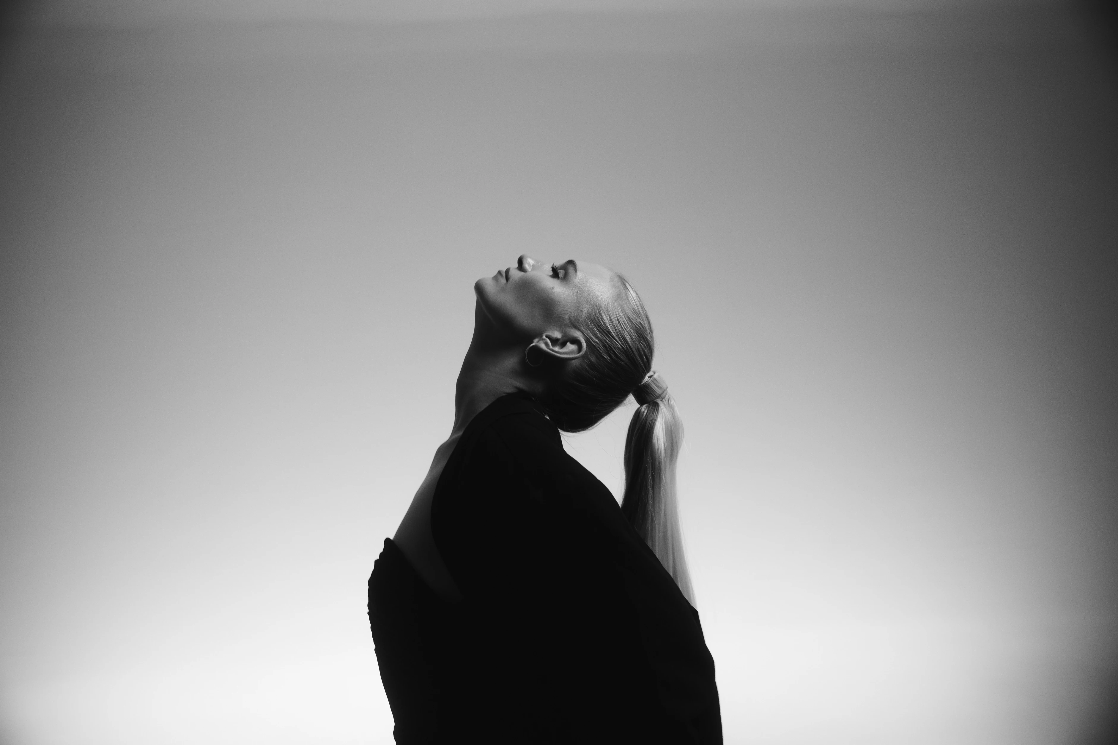 Schwarz-weiß Porträt einer Frau mit zurückgelegtem Kopf vor minimalistischem Hintergrund.