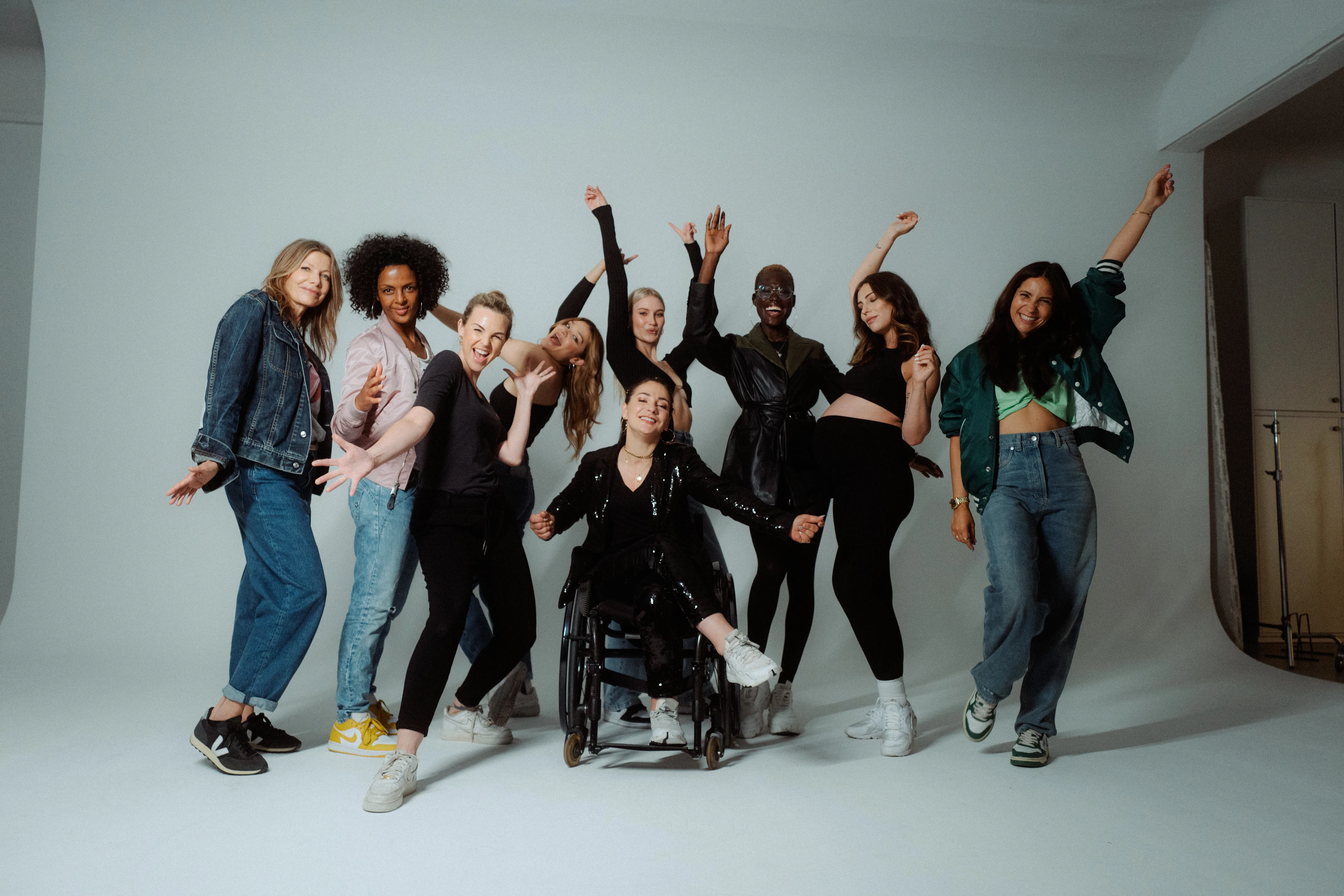 Gruppe von Frauen tanzt und feiert gemeinsam im Studio, eine Frau im Rollstuhl im Mittelpunkt.