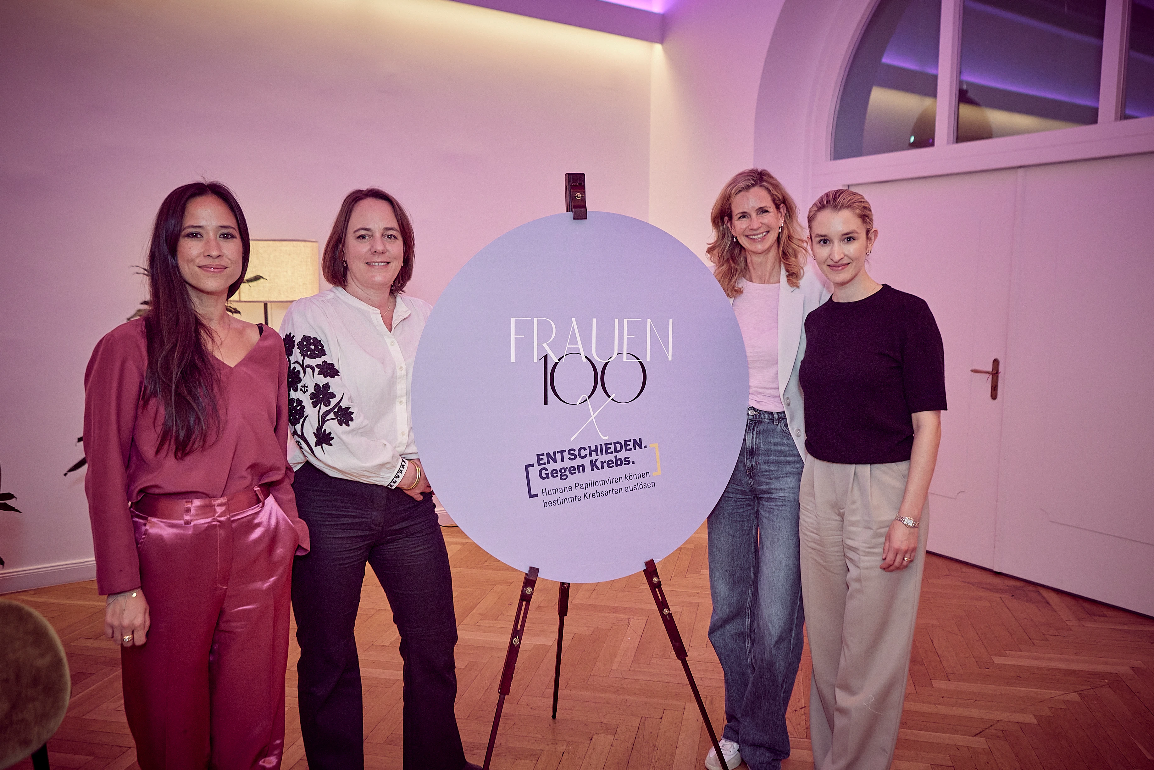 Vier Frauen stehen neben einem großen „Frauen 100“-Schild und posieren für ein Foto – ein klarer, selbstbewusster Abschlussmoment mit Event-Branding.