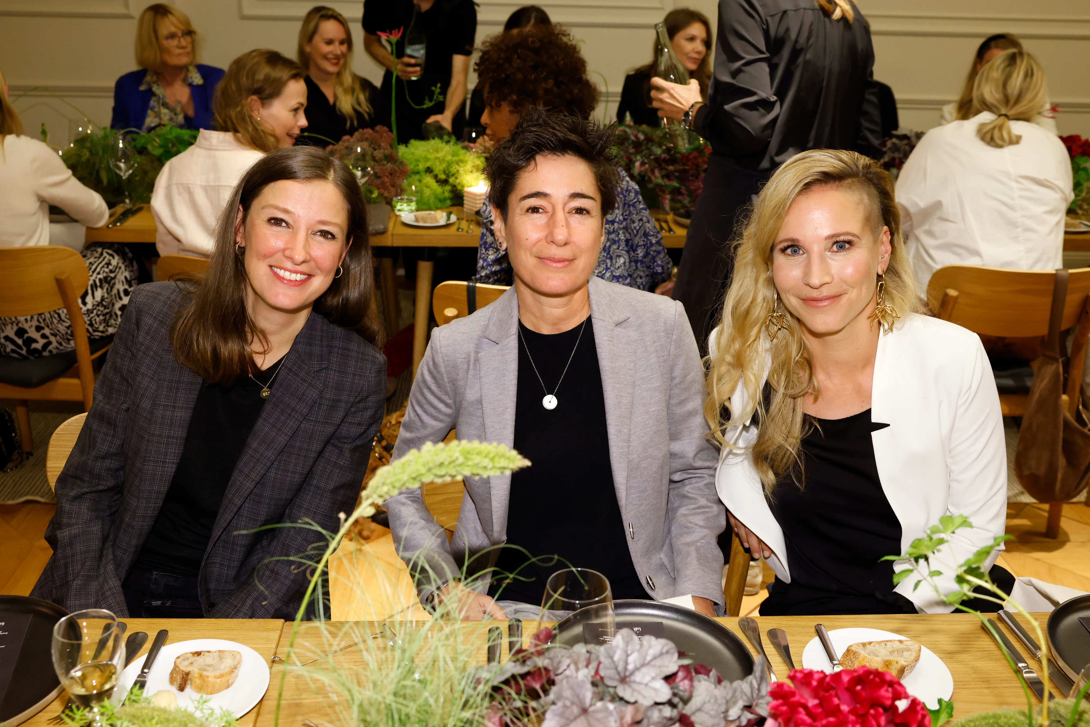Drei Frauen sitzen nebeneinander am Tisch und schauen lächelnd in die Kamera.