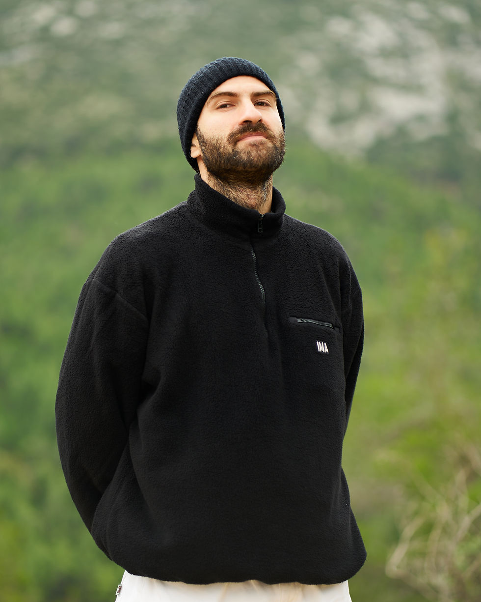 Thumbnail: Irregular Movement of Arts: Andi Xhuma wearing the I.M.A Fleece, in black, which features an embroidery design on the back.