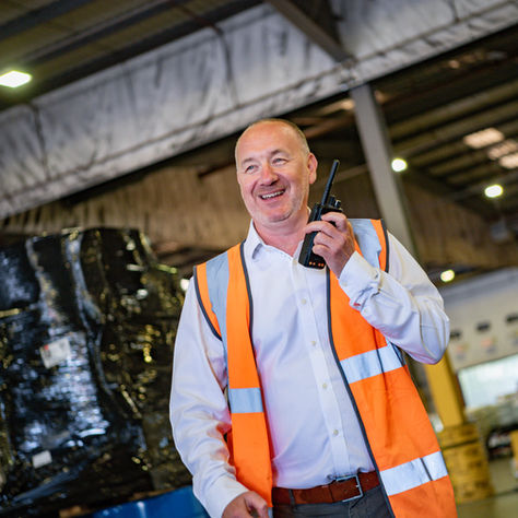 A logistics manager walking through a warehouse whilst talking on a radio.