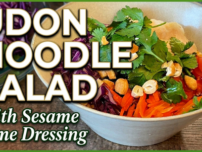 A bowl of udon noodles topped with colorful vegetables, protein, and cashews.