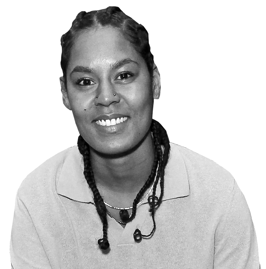 A black and white picture of Char. She has dark skin and long dark hair that is styled in cornrows. She is smiling and wearing a white collared shirt and two necklaces.