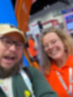 Two smiling attendees take a selfie at a ClassVR booth at a tech expo, with colorful signs and displays behind them.