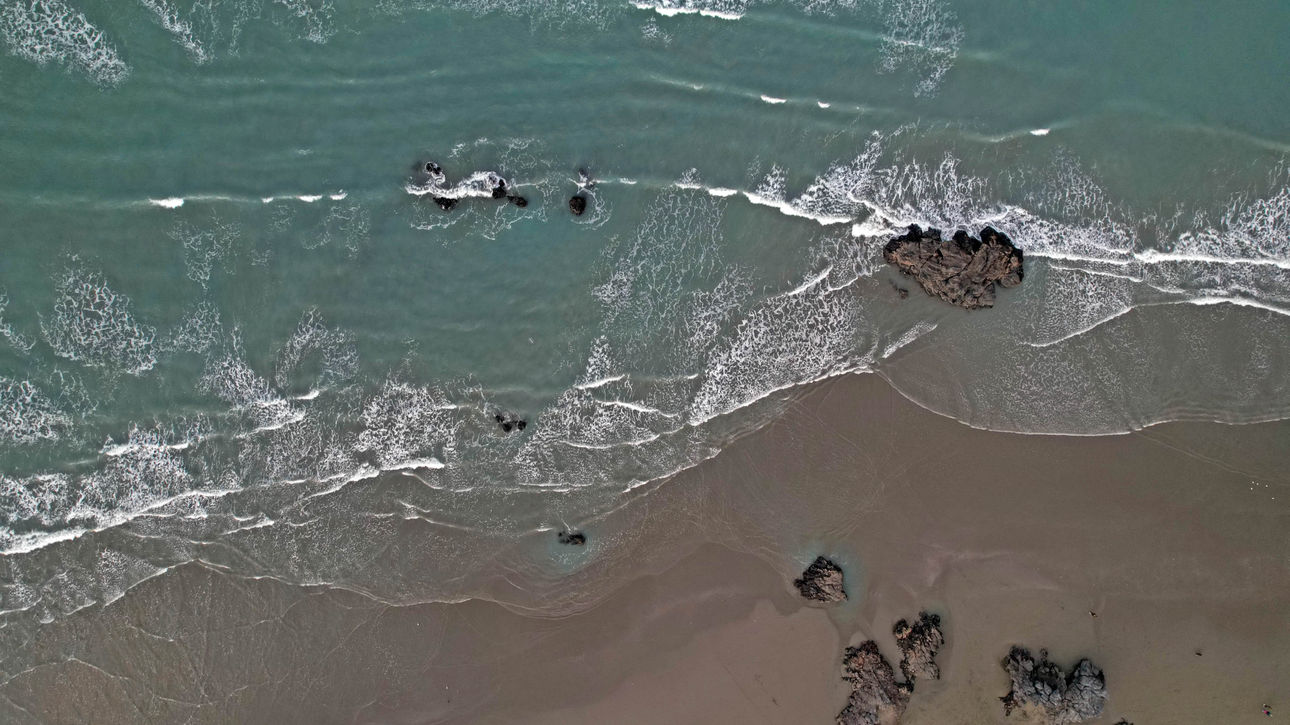 Aerial view of Sumner Beach showing golden sand, scattered rocks, and blue-green ocean gradient.