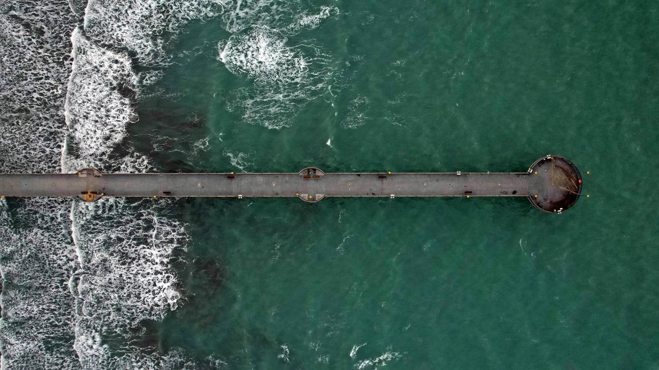 View of New Brighton Pier's circular end at night with crashing waves and orange lamppost glow.