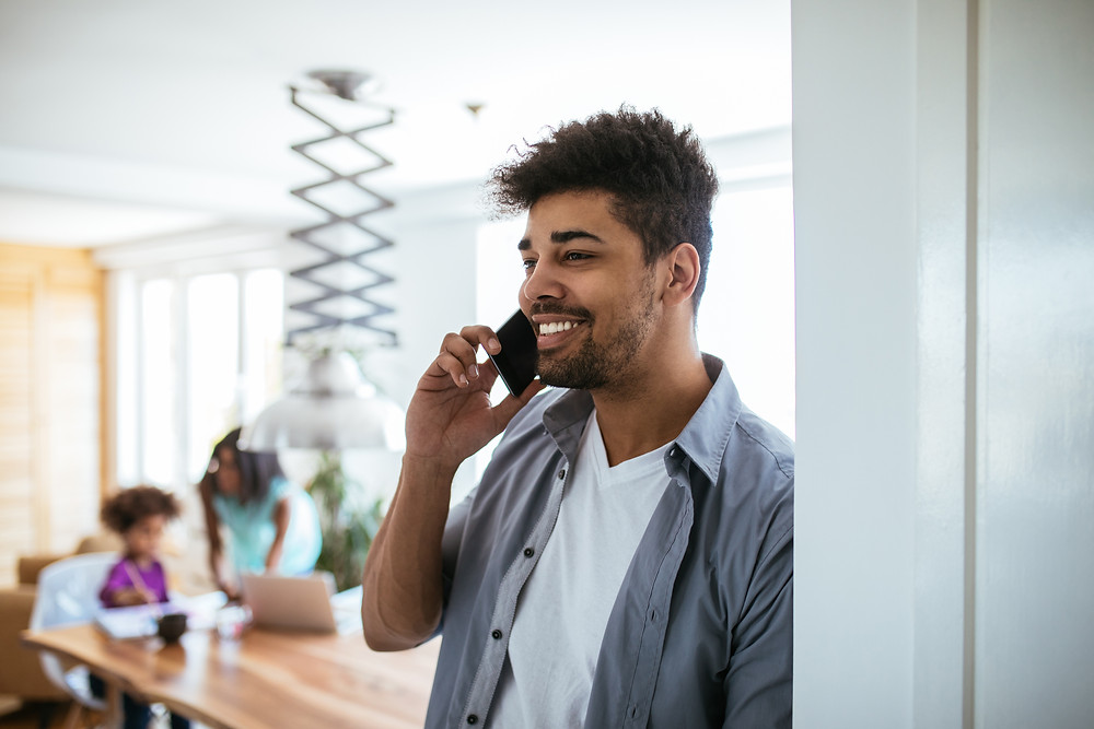 Father stands in kitchen while talking on the phone to set up an insurance review appointment with his agent.
