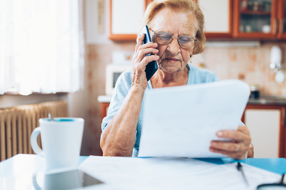 Elderly woman looks at her insurance policy as she speaks on the phone to her agent.